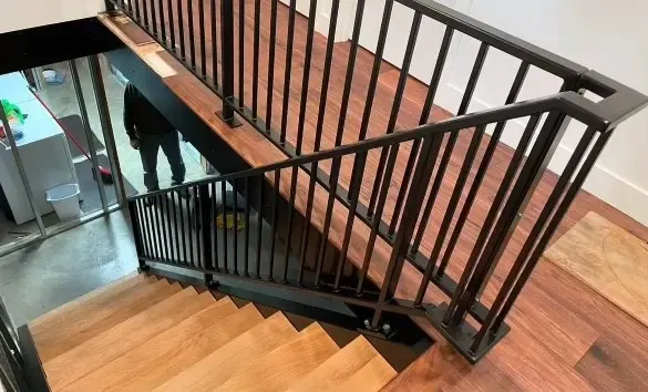 Black powder-coated steel stair railing installed over wood treads